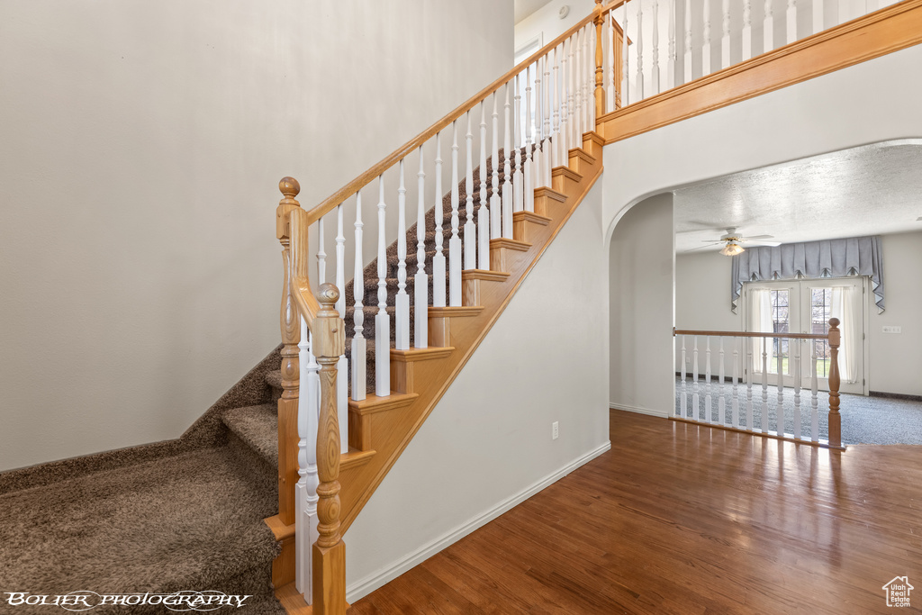 Stairway with wood finished floors, arched walkways, baseboards, ceiling fan, and french doors