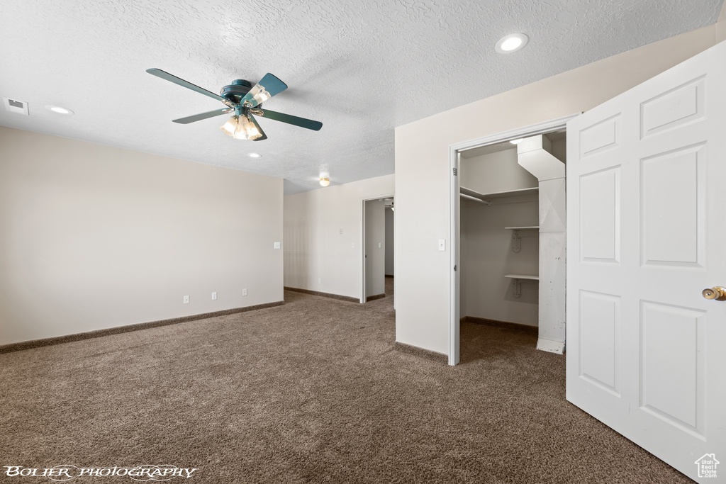 Unfurnished bedroom with carpet flooring, a spacious closet, a textured ceiling, baseboards, and a closet