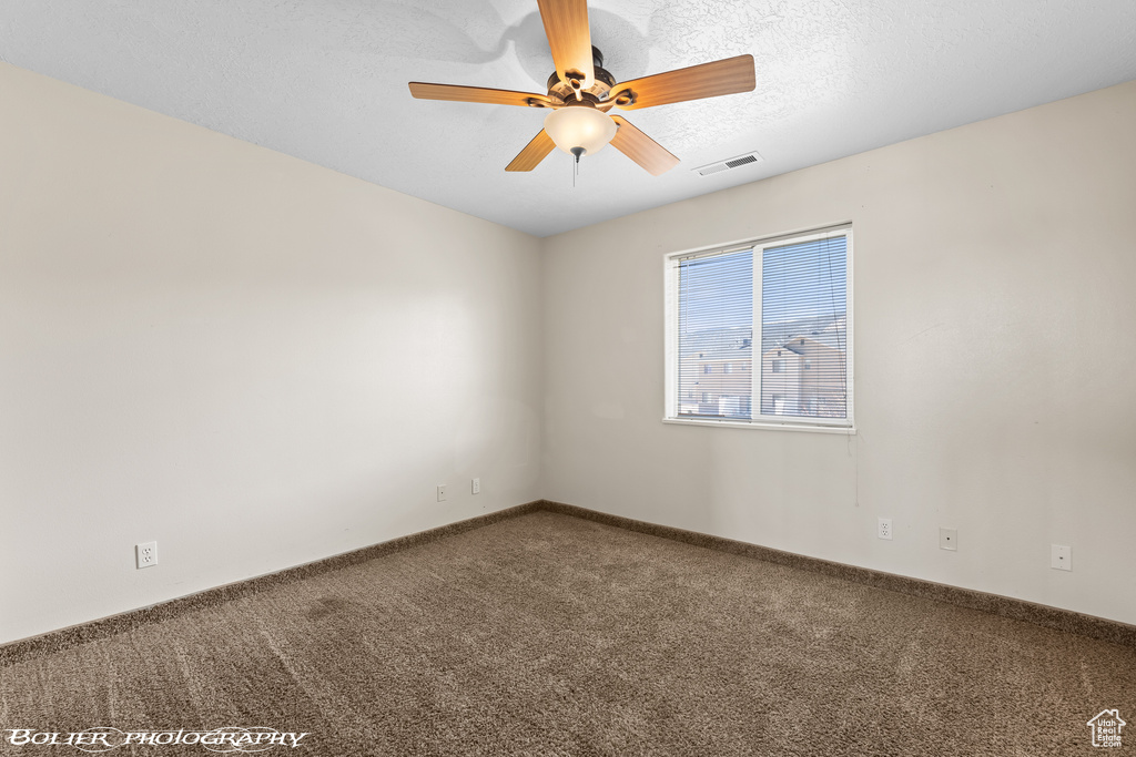 Carpeted spare room with ceiling fan, baseboards, and a textured ceiling