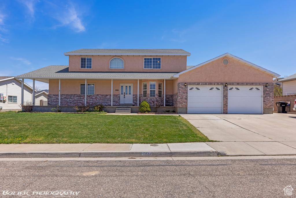 View of front facade featuring stucco siding, an attached garage, driveway, a front lawn, and a porch