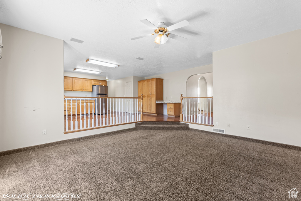 Unfurnished room featuring a ceiling fan, dark colored carpet, and baseboards