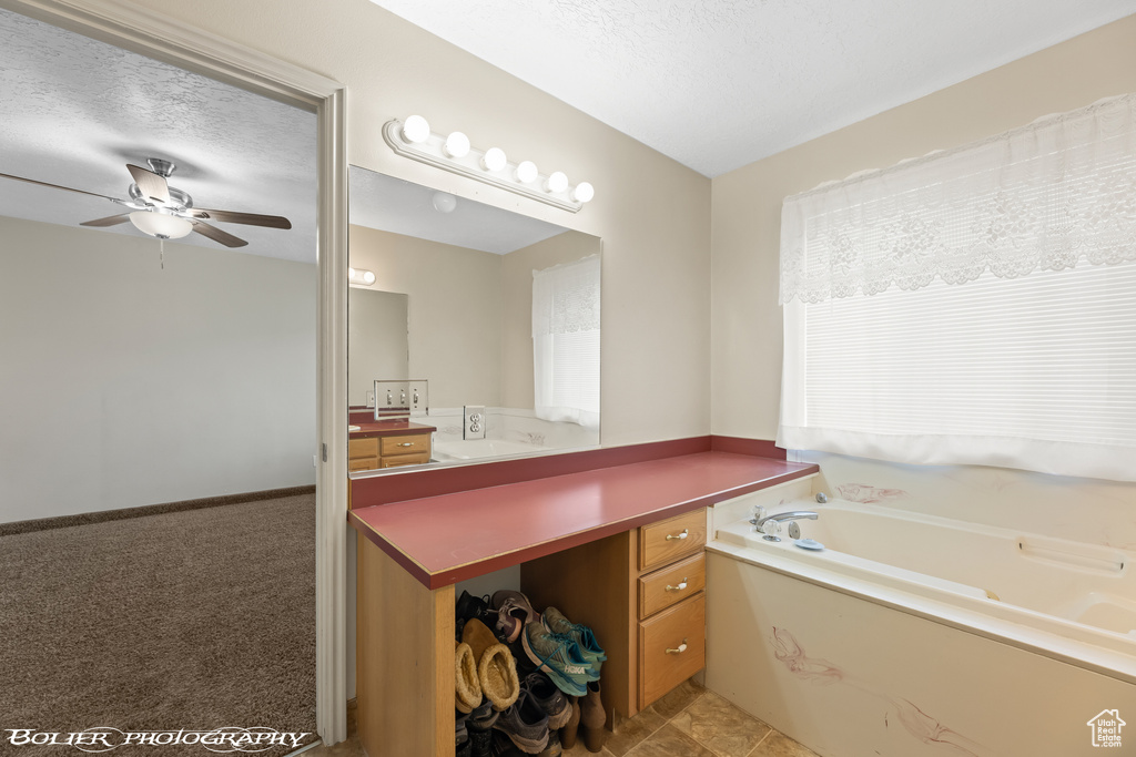Full bathroom featuring a ceiling fan, a garden tub, vanity, and a textured ceiling