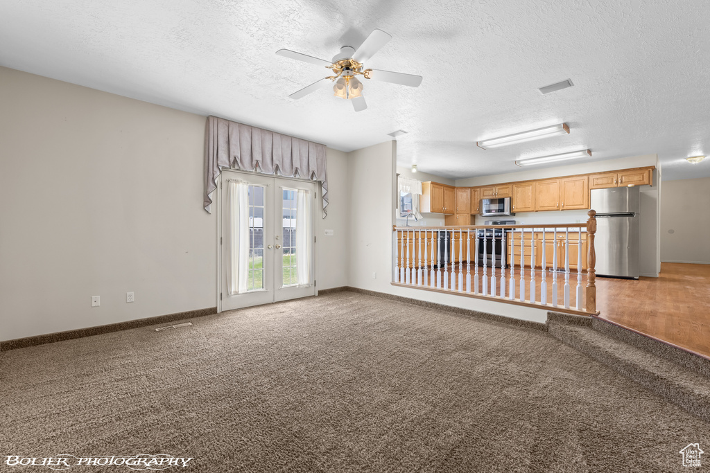 Unfurnished living room featuring a textured ceiling, light carpet, a ceiling fan, french doors, and baseboards