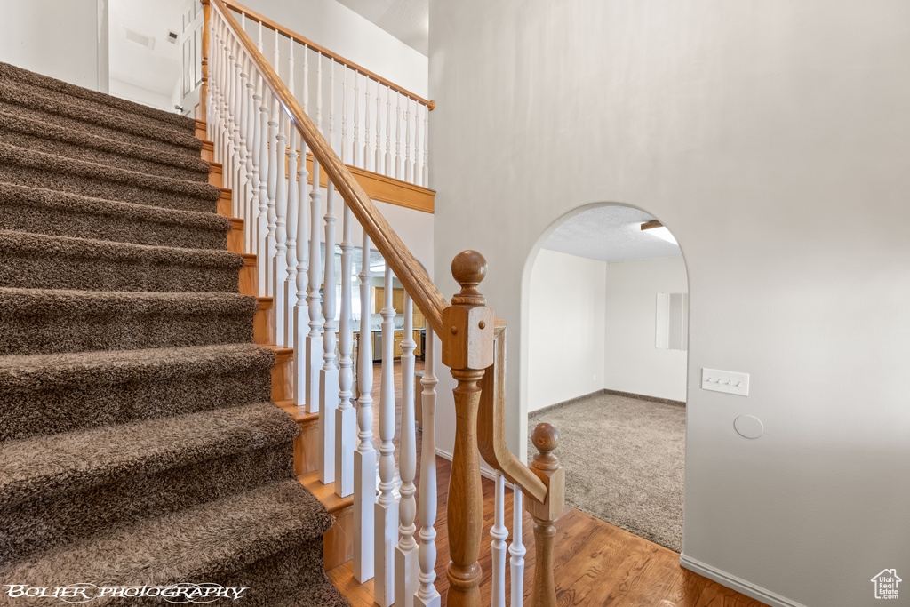 Staircase featuring arched walkways, wood finished floors, baseboards, and a towering ceiling