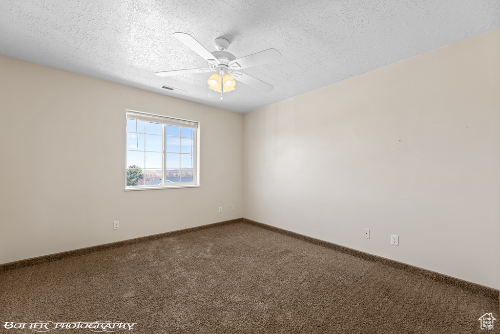 Carpeted spare room featuring a textured ceiling, ceiling fan, and baseboards