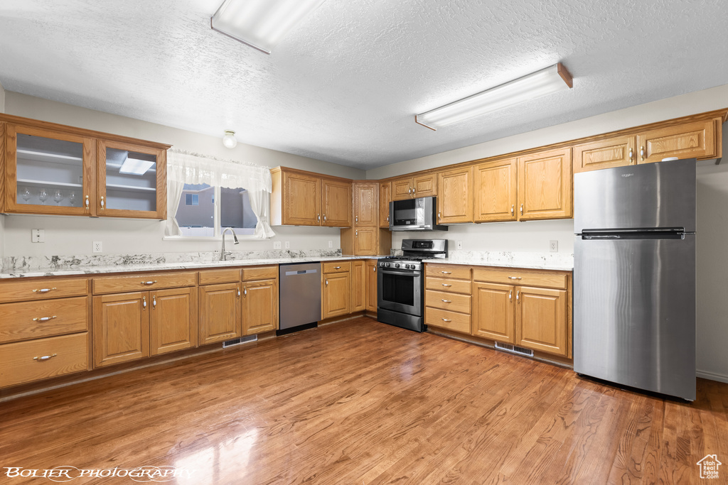 Kitchen with appliances with stainless steel finishes, a textured ceiling, light countertops, light wood-style flooring, and glass insert cabinets