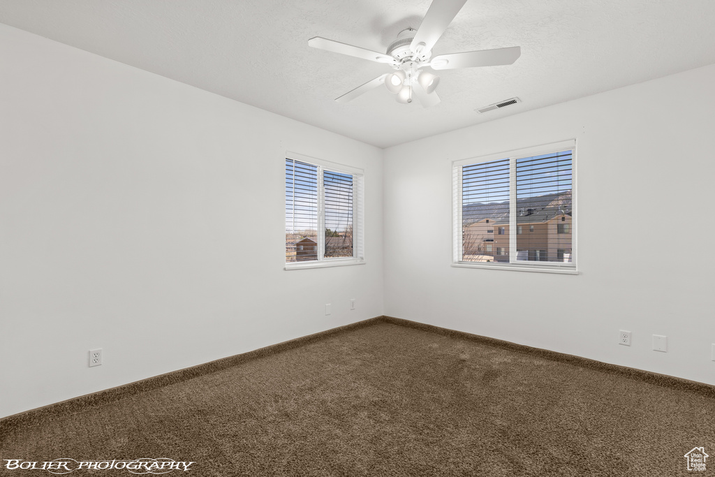 Unfurnished room featuring dark carpet, a ceiling fan, healthy amount of natural light, and baseboards