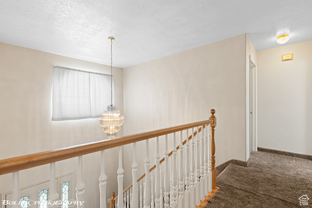 Corridor featuring an upstairs landing, carpet, a chandelier, a textured ceiling, and baseboards