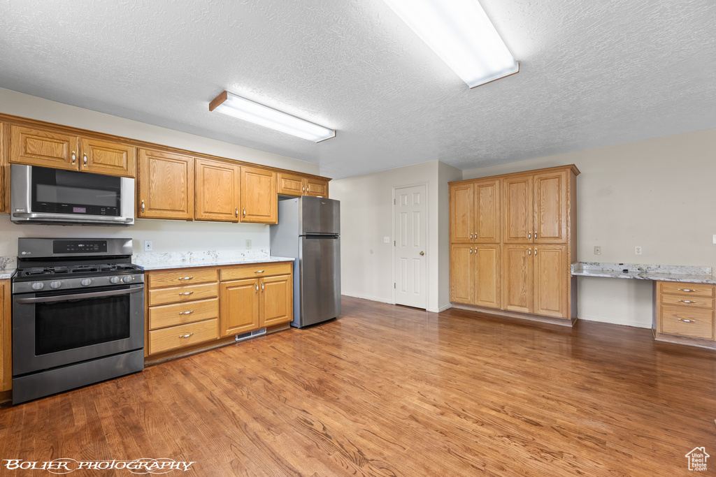 Kitchen featuring stainless steel appliances, a textured ceiling, wood finished floors, and brown cabinetry