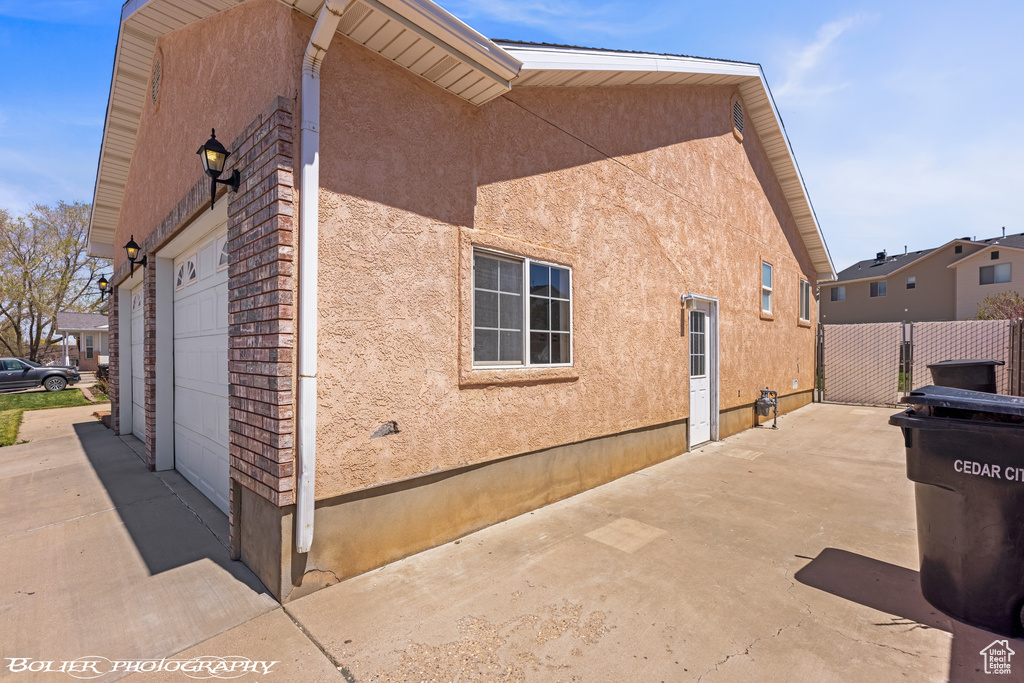 View of side of property featuring an attached garage, stucco siding, fence, driveway, and a patio area