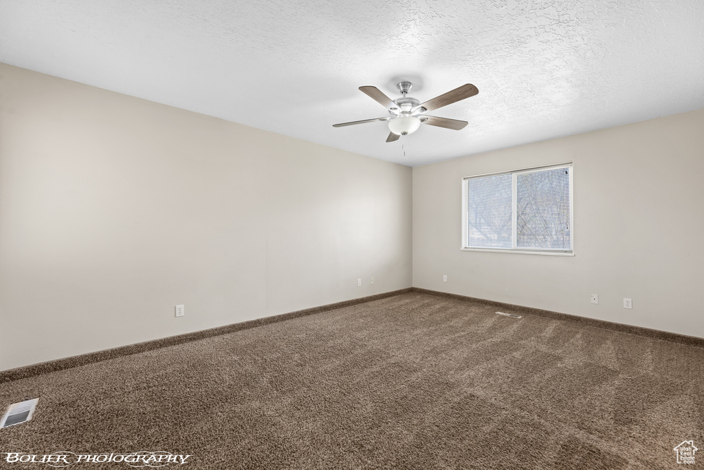 Carpeted empty room with a ceiling fan, a textured ceiling, and baseboards