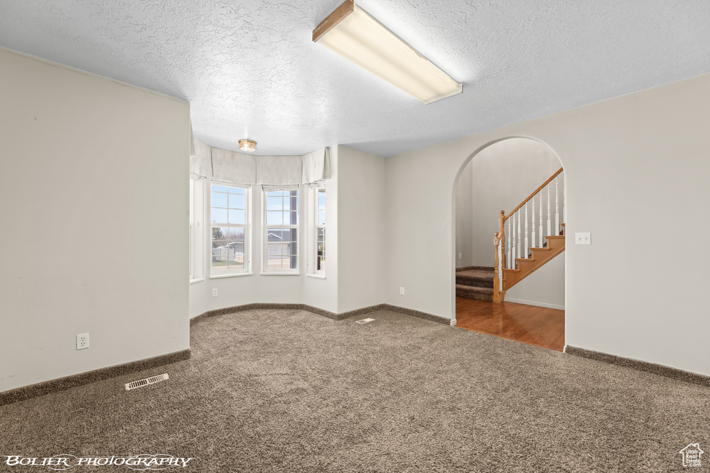 Carpeted spare room featuring a textured ceiling, arched walkways, stairway, and baseboards