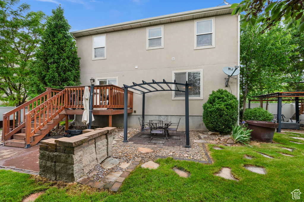 Back of property with a pergola, a deck, a yard, a patio area, and stucco siding
