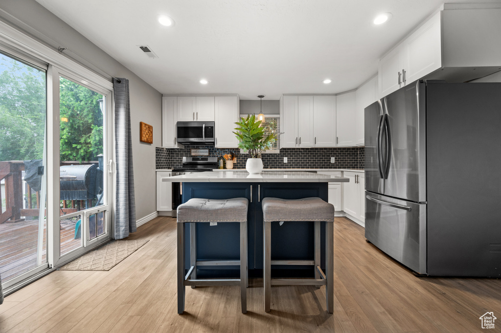 Kitchen featuring stainless steel appliances, light countertops, white cabinets, light wood-type flooring, and backsplash