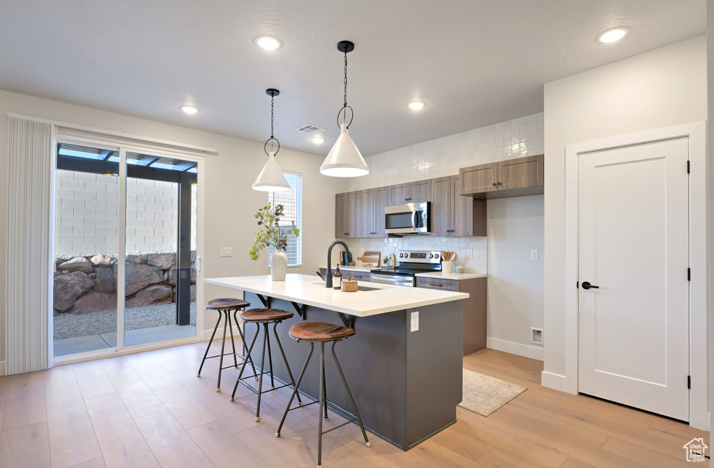 Kitchen featuring stainless steel appliances, a sink, light countertops, light wood-style floors, and decorative backsplash
