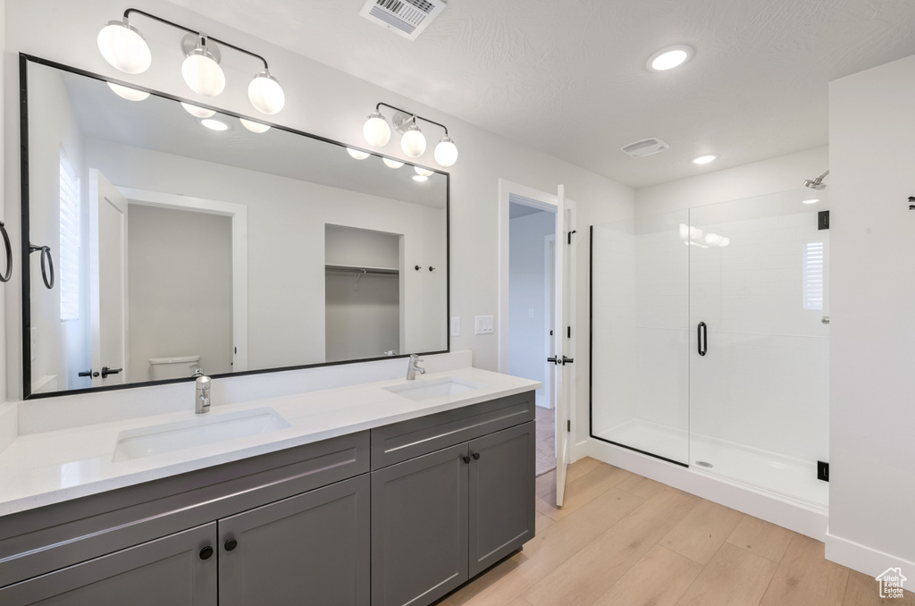 Full bath with a shower stall, wood finished floors, toilet, double vanity, and recessed lighting