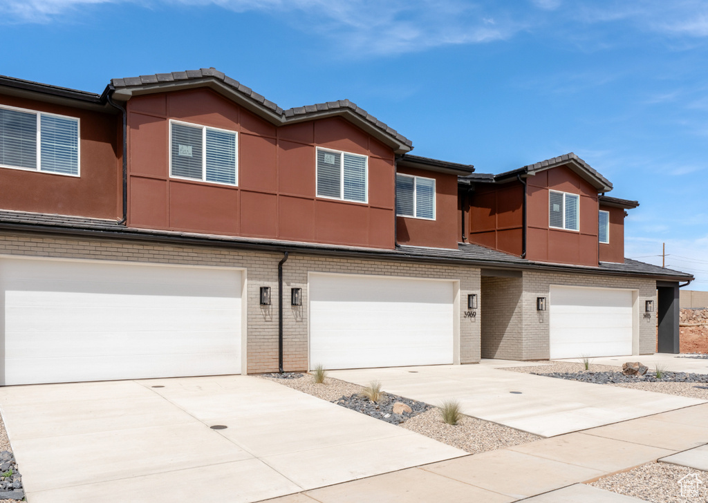 Townhome / multi-family property featuring an attached garage, concrete driveway, a tiled roof, and stucco siding