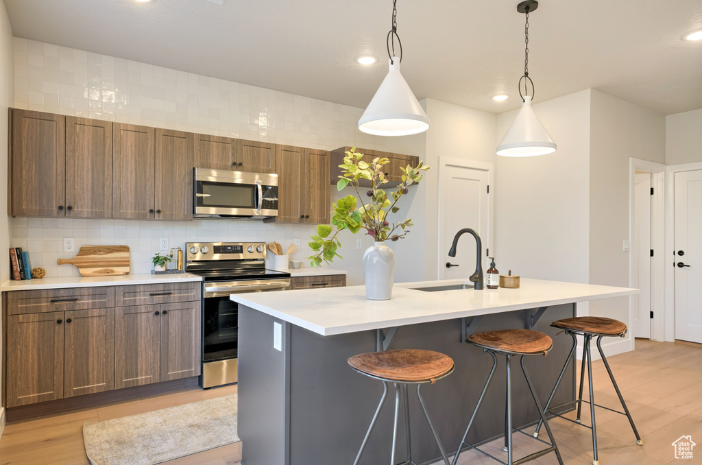Kitchen with stainless steel appliances, a sink, light wood-type flooring, a kitchen breakfast bar, and recessed lighting