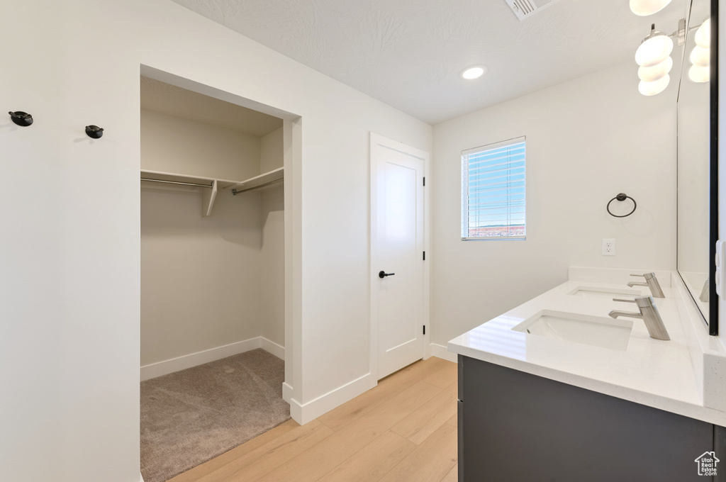 Bathroom with wood finished floors, baseboards, double vanity, a spacious closet, and recessed lighting