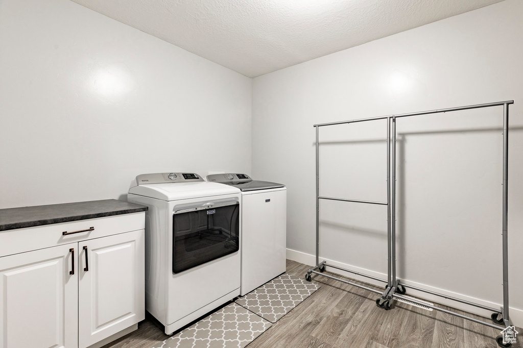 Laundry room featuring washer and clothes dryer, light wood-style floors, cabinet space, a textured ceiling, and baseboards
