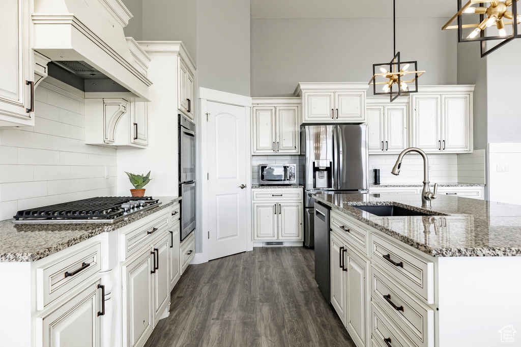 Kitchen featuring stainless steel appliances, a sink, a chandelier, decorative backsplash, and custom range hood