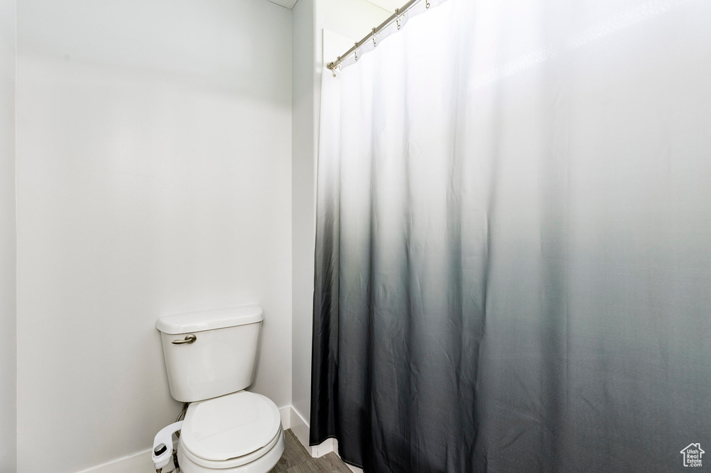 Bathroom with baseboards, toilet, a shower with curtain, and wood finished floors