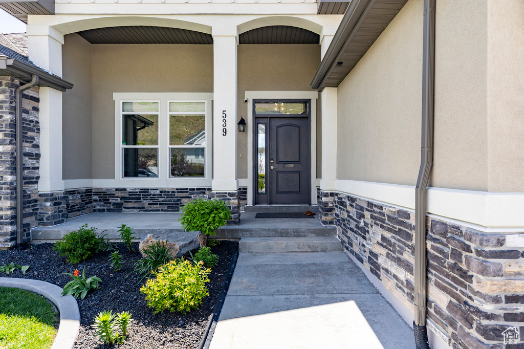 View of exterior entry with a porch, stucco siding, and stone siding
