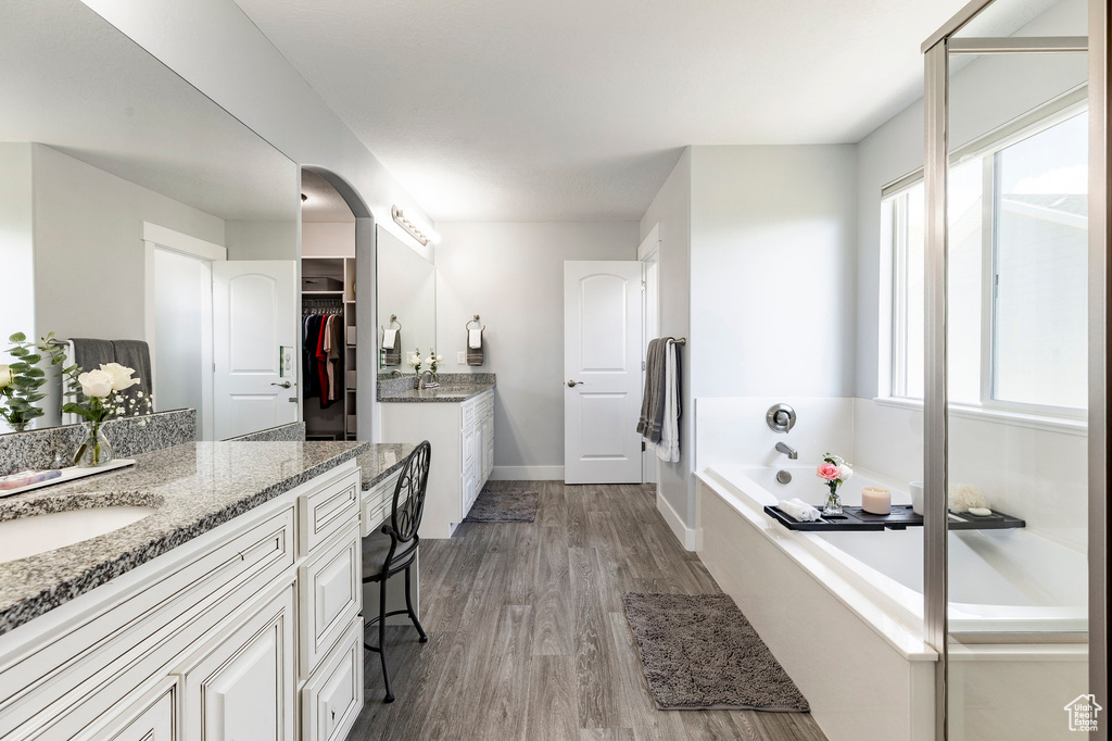 Bathroom with two vanities, wood finished floors, a bath, baseboards, and a walk in closet