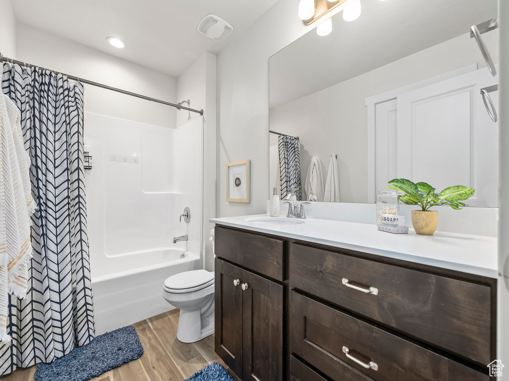 Bathroom featuring wood finished floors, vanity, toilet, and shower / bathtub combination with curtain