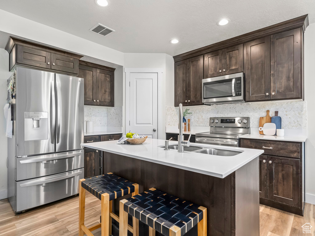 Kitchen with appliances with stainless steel finishes, dark brown cabinetry, light wood-type flooring, light countertops, and recessed lighting