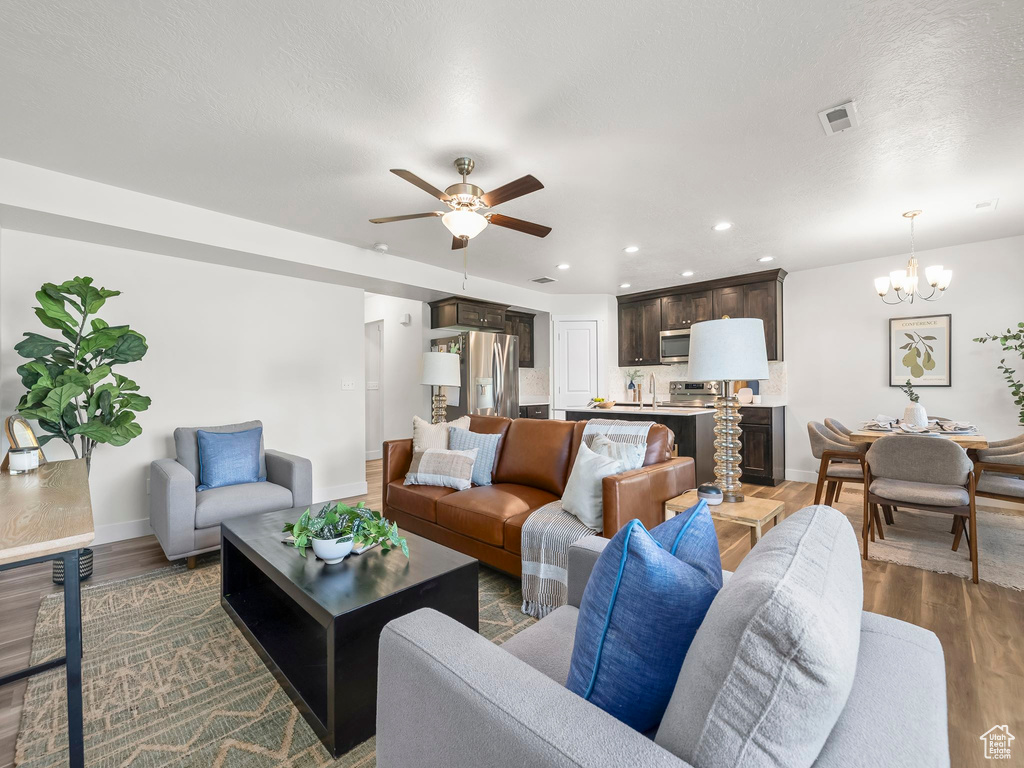 Living room with a chandelier, baseboards, wood finished floors, a ceiling fan, and recessed lighting