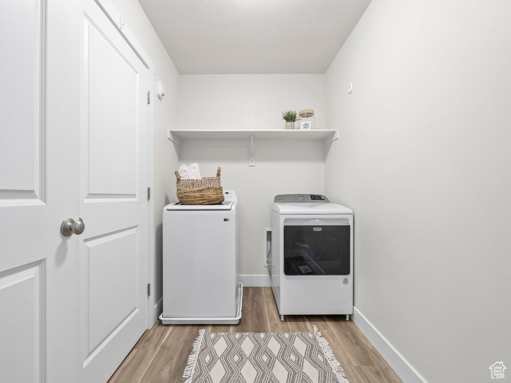 Clothes washing area featuring washer and clothes dryer, light wood-style flooring, and baseboards