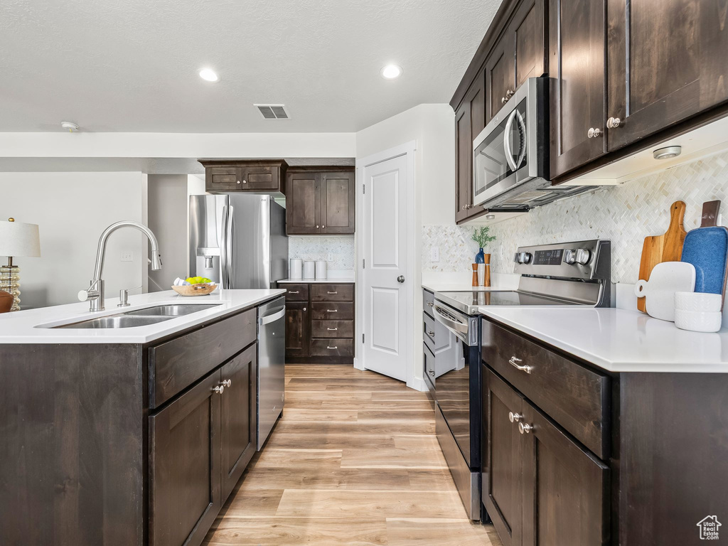 Kitchen with appliances with stainless steel finishes, a sink, light wood-type flooring, dark brown cabinets, and light countertops