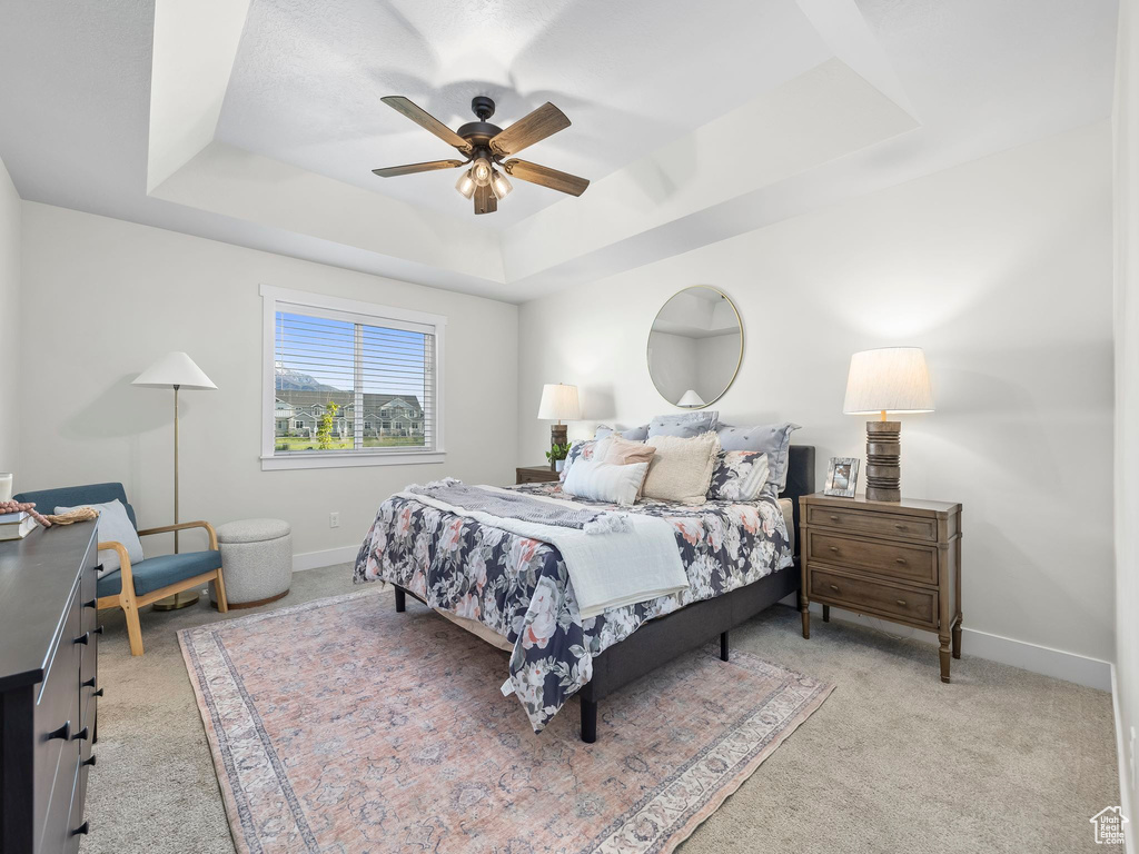 Bedroom featuring a tray ceiling, light carpet, baseboards, and ceiling fan