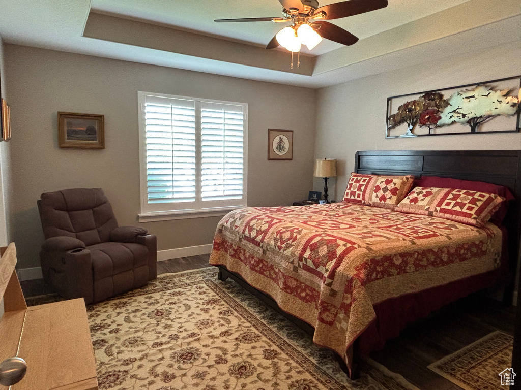 Bedroom featuring baseboards, wood finished floors, a tray ceiling, and ceiling fan