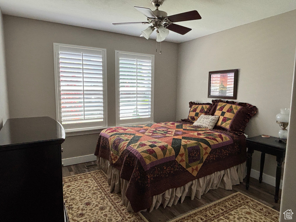 Bedroom with wood finished floors, baseboards, multiple windows, and ceiling fan