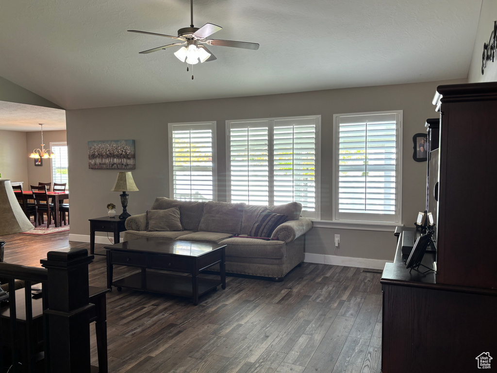 Living room featuring dark wood-style floors, ceiling fan, baseboards, a chandelier, and vaulted ceiling