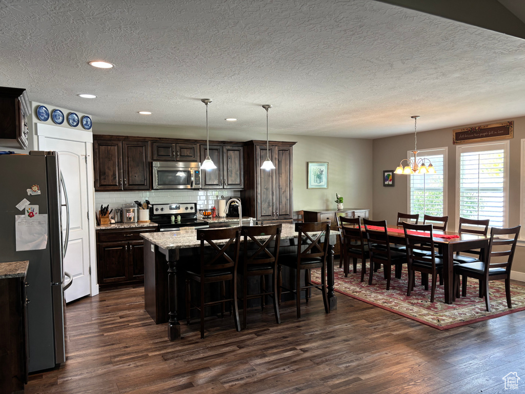 Kitchen featuring appliances with stainless steel finishes, dark wood-type flooring, a breakfast bar, a textured ceiling, and dark brown cabinets