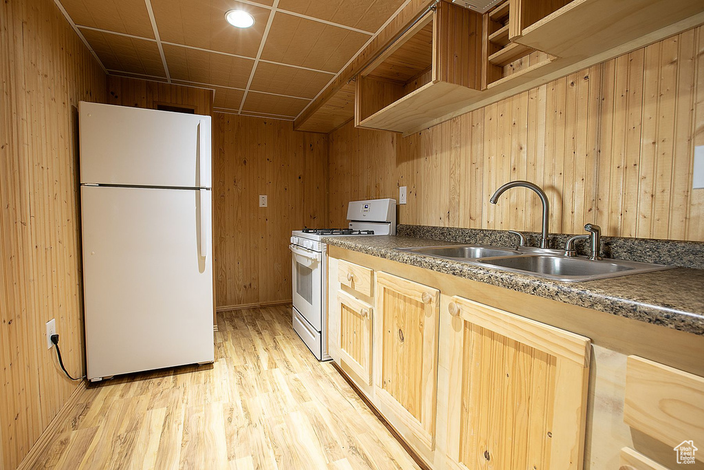 Kitchen featuring white appliances, a sink, wooden walls, light wood-style floors, and dark countertops