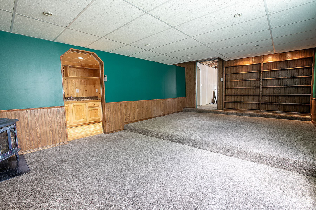 Unfurnished living room with a wood stove, wainscoting, wood walls, built in shelves, and carpet floors