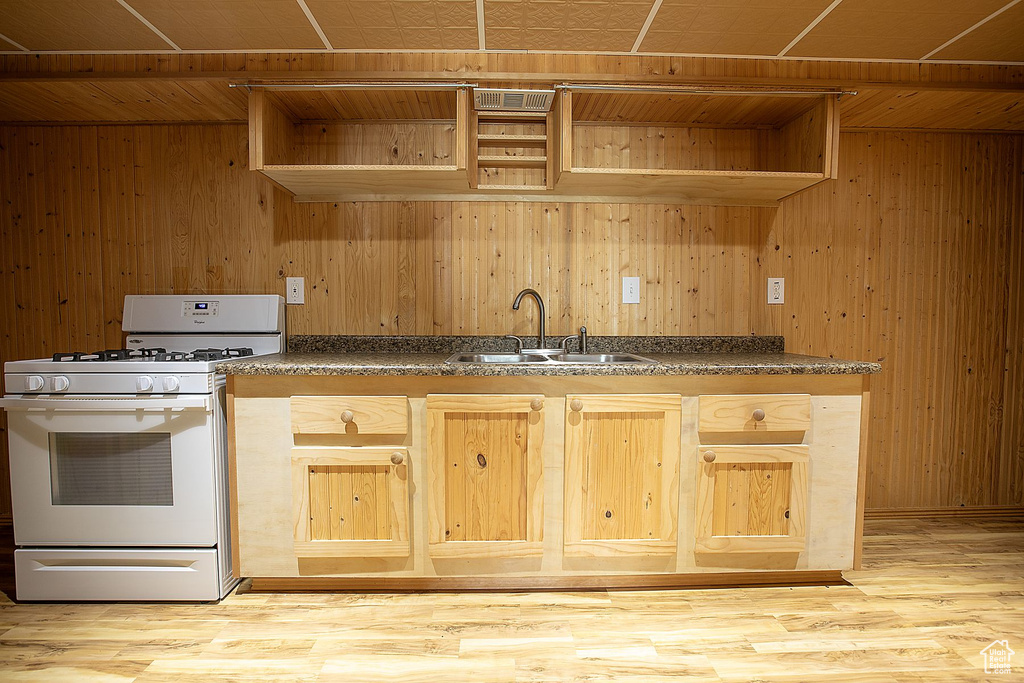 Kitchen featuring gas range gas stove, a sink, open shelves, wooden walls, and dark countertops