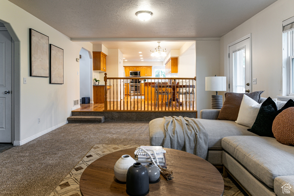 Living room featuring carpet, a chandelier, baseboards, arched walkways, and a textured ceiling