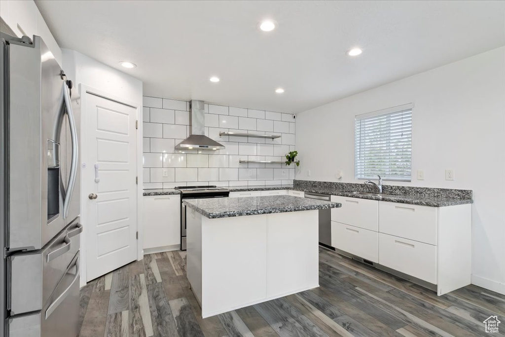 Kitchen featuring appliances with stainless steel finishes, wall chimney exhaust hood, decorative backsplash, a kitchen island, and dark stone counters