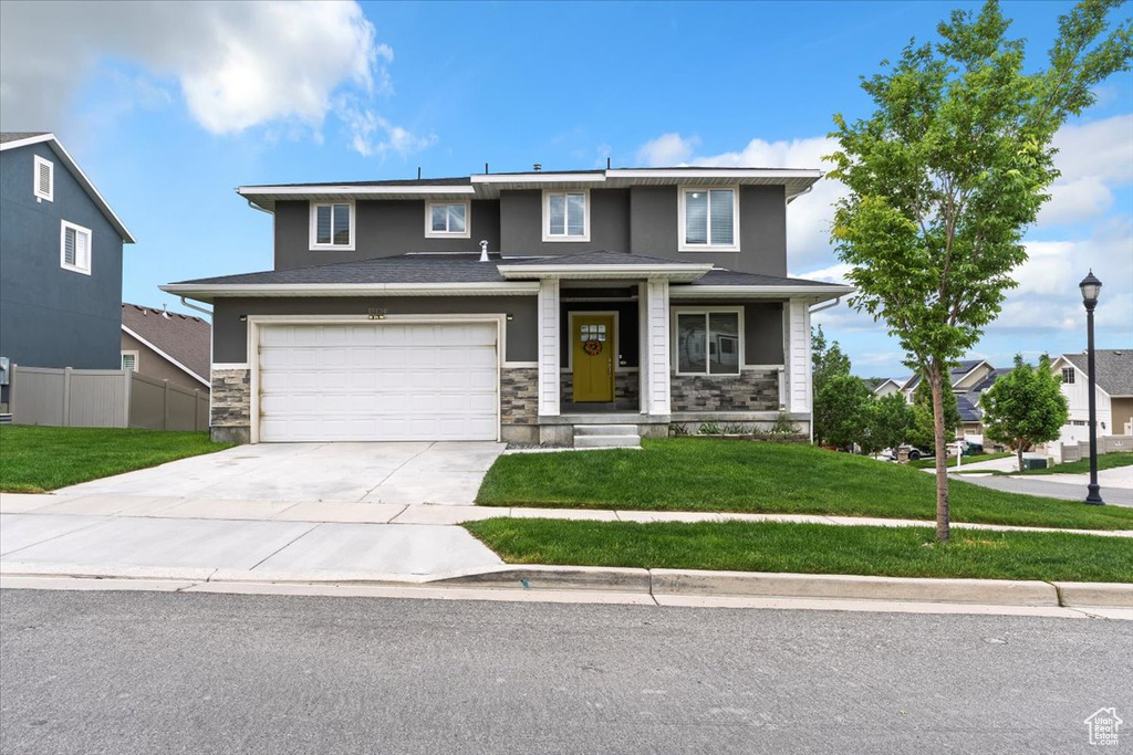 View of front of property with driveway, stone siding, a garage, and covered porch