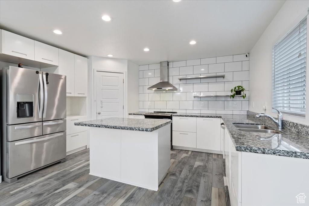 Kitchen featuring stainless steel appliances, wall chimney exhaust hood, a sink, open shelves, and wood finished floors