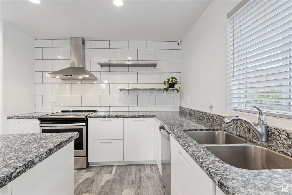 Kitchen featuring wall chimney exhaust hood, appliances with stainless steel finishes, a sink, dark stone counters, and white cabinets