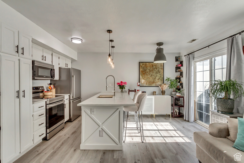 Kitchen with stainless steel appliances, light wood-style floors, a sink, white cabinets, and light countertops