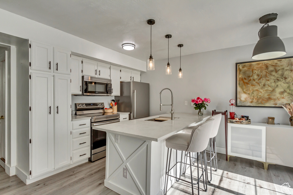 Kitchen with appliances with stainless steel finishes, a sink, light wood-style floors, and white cabinets