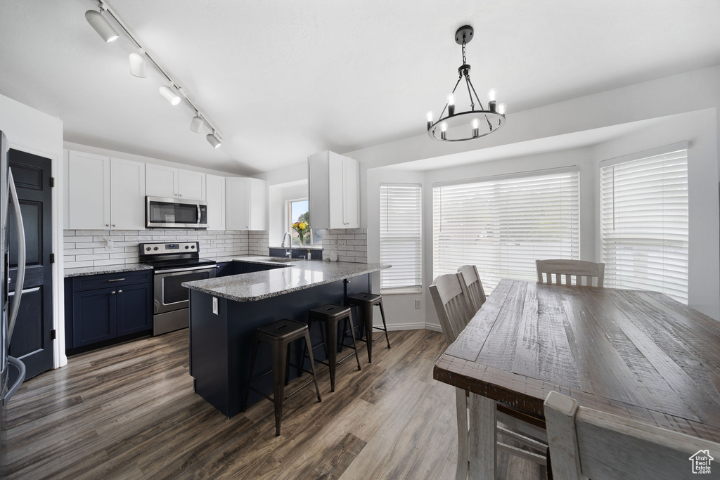 Kitchen featuring appliances with stainless steel finishes, a breakfast bar, a sink, white cabinets, and a chandelier