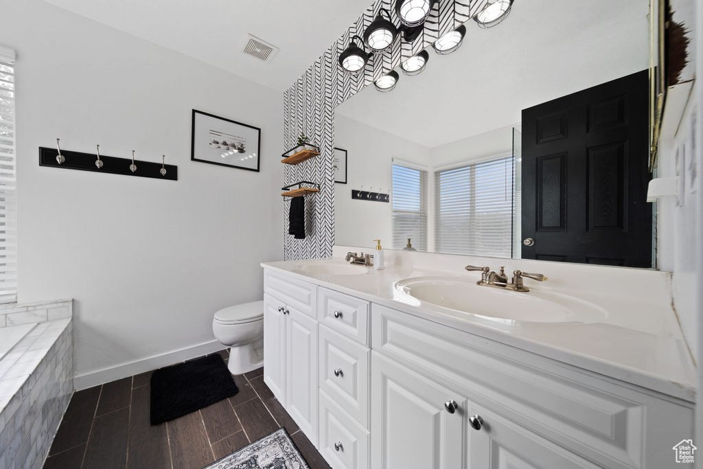 Full bath with double vanity, toilet, baseboards, and a tub